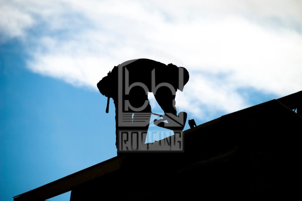 Silhouette of a roofer working on a roof under a clear blue sky.